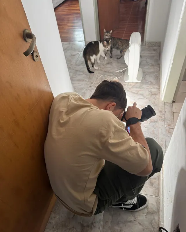 Santi filmando agachado en un pasillo, con dos gatos mirando